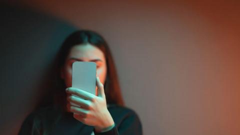 A girl with long brown hair looking at a phone - her face is obscured by the phone