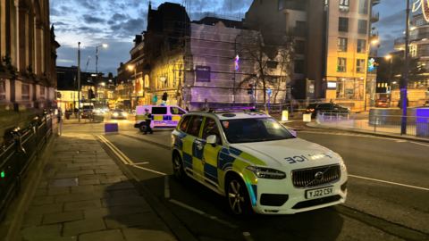 Great George Street in Leeds with a police cordon tape and two police vehicles, one van and one car. 