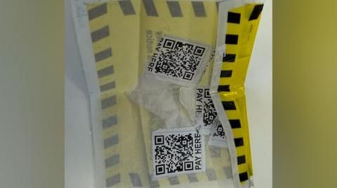 A yellow and black label with three QR codes on the reverse side. The QR codes say "PAY HERE" in capital letters at the bottom.