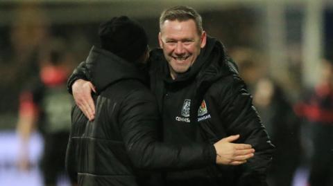 Kevin Nolan hugs a member of the Northampton coaching staff following the win at Mansfield