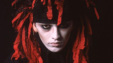 A young Pete Burns in red and black headwear with white face and dark eye make up