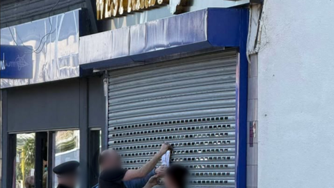 Image shows enforcement officers putting a closure order notice on the metal grilles on the outside of the West Kirby Vape Shop