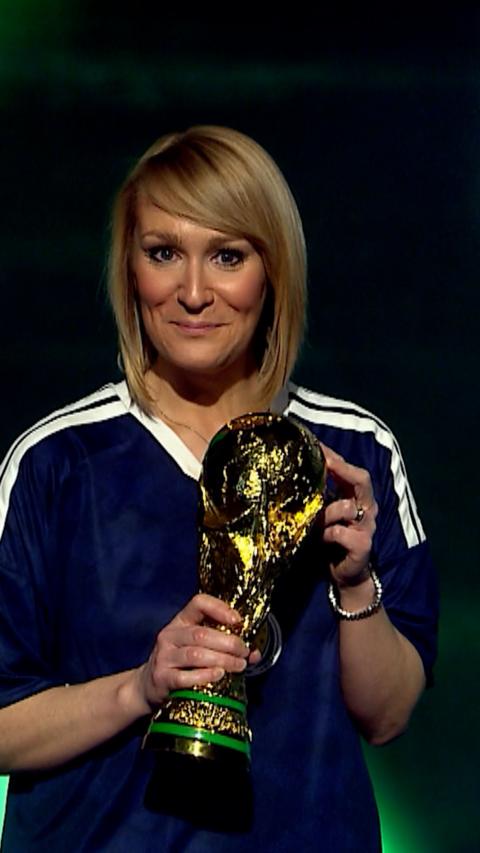 Weather presenter Kirsteen Macdonald smiles at the camera as she holds a fake world cup trophy. She has blonde hair and is wearing a Scotland football top.
