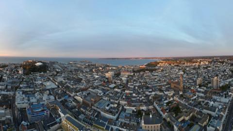A fish eye lens view of St Hellier in Jersey showing churches housing and buildings and the sea in the background