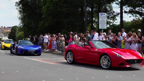 Supercars drive down a crowd-lined road