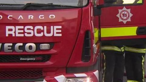 A fire truck front with the door open and two firefighters visible.