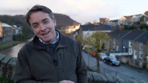 Jonah Fisher standing on a bridge in a Welsh town.