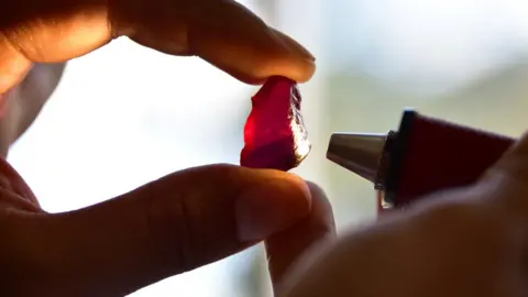 A worker examines a large ruby at a mine in Mozambique. Stock photo.