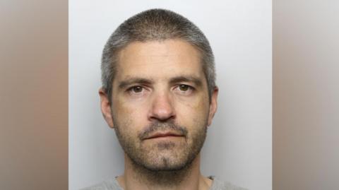 A police mugshot of Lee Boocock, who has shaved grey hair and grey stubble.