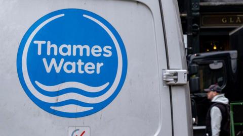 A generic picture of a white Thames Water van with its logo on the back, with a man walking past it wearing a grey hooded jumper, a black gilet and a black cap.