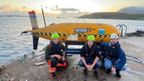 Boaty McBoatface with three engineers on a quayside on Isle of Harris