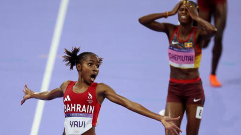 Winfred Yavi spreads her arms wide in celebration as she crosses the steeplechase finish line with Peruth Chemutai in the background behind her covering her face in the agony of defeat