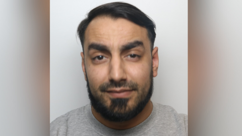 A mugshot of Mohammed Sardar wearing a grey sweatshirt. He has short dark hair and dark facial hair 