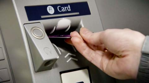 A hand putting a card into a cash machine