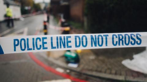 Photo of the white and blue police cordon tape and the mess on the street in the background, in the place of the crime scene. (stock image)