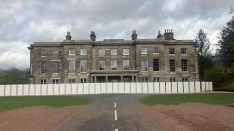 Photograph of Haigh Hall in Wigan. The image shows wooden boarding surrounding the mansion due to restoration work.