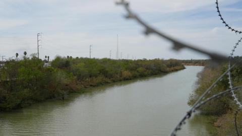 The Rio Grande river - near the Mexican city of Reynosa near the US border - is seen behind blurred spikes of barbed wire. 