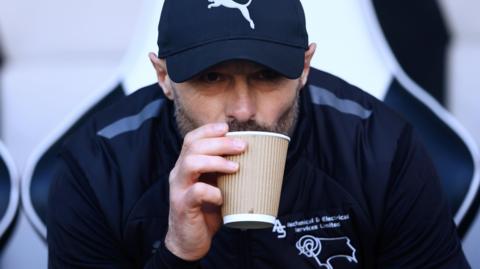 Paul Warne sipping a hot drink under a baseball cap