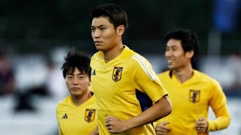 Three people wearing yellow Japan jerseys on a football field