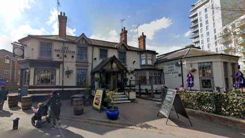 A pub building with two A-board signs outside. The pub has a sign on the wall reading "THE SOVEREIGNS".