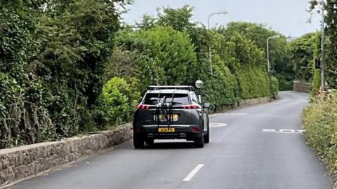 Route de Noirmont. A narrow road with trees and bushes either side. The picture shows the white lines running along the road until they stop and don't go any further. 