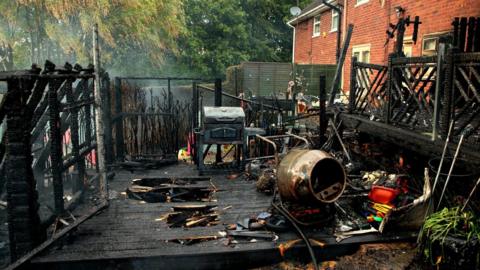The charred remains of a veranda ravaged by fire. Several items have been damaged by fire, including a cement mixer and a barbeque.