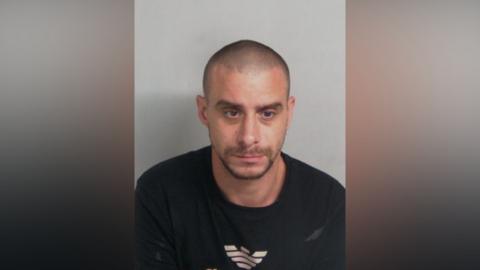Custody photo of a man. He is wearing a black jumper and not looking at the camera 