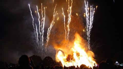 Crowd around a bonfire watching a firework display