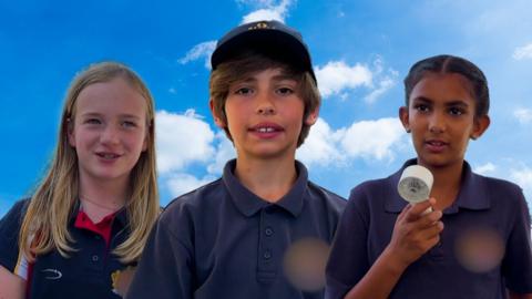 Three children stand in their school uniforms face on to the camera.