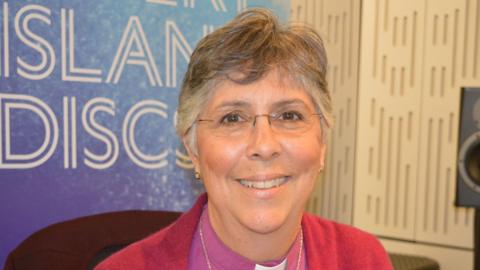 Guli Francis-Dehqani, who is wearing a pink cardigan, smiling at the camera. She is in the Desert Island Discs radio studio. She has grey hair and is wearing glasses.