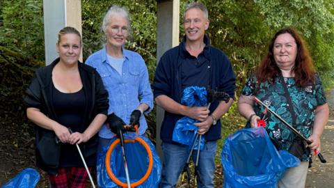 A group of women and a man holding litter-picking equipment
