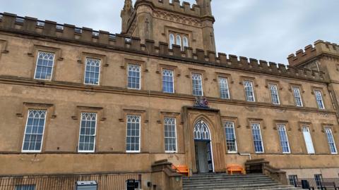 The exterior of Elizabeth College. There are tall windows and towers which make it look like a castle.