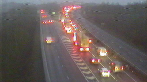 A traffic camera captures drivers heading away into the distance. The vehicles' red tail lights are captured as they wait in queues.
