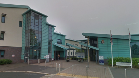 A blue and white hospital building with Union Jack and England flags outside. 