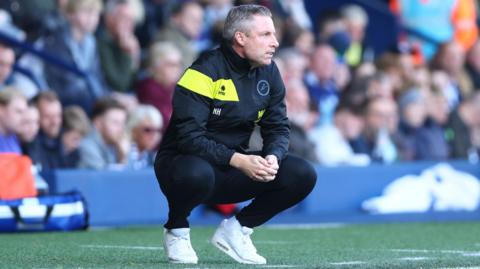 Neil Harris crouches down as he watches from the touchline