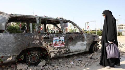 A veiled Iranian woman stands next to an ambulance of the Iranian Red Crescent Society (IRCS) that was destroyed in an Israeli strike, in Tehran, Iran, 23 June 2025.