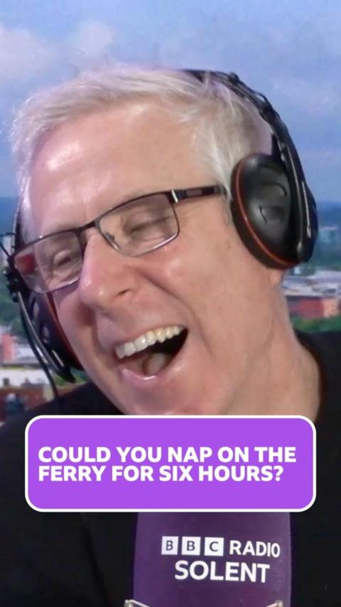 Alun Newman has short white hair and headphones on. He wears rectangular black wire framed glasses and his mouth is open mid-laugh.