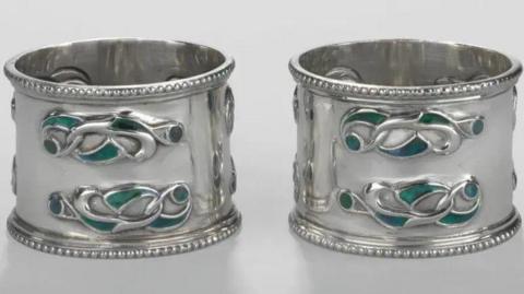Two small, round silver pieces featuring Celtic-inspired designs in green and blue.