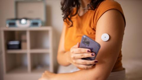 Young diabetic patient monitoring glucose level with remote sensor at home, she has a glucose monitor on her arm