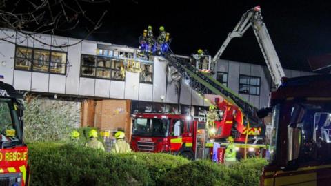 Fire crews and fire engines at an industrial building at night.