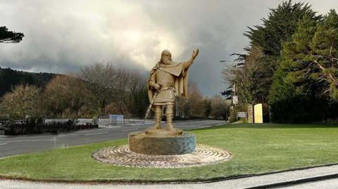 An artist's impression of a large bronze sculpture of King Orry. He is wearing a cape, carries a sword in one hand, and has his other arm stretched out.