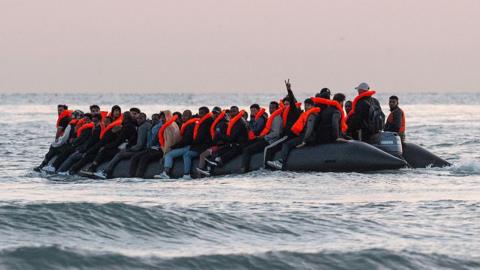 A man gestures from a dinghy as migrants prepare to sail into the English Channel on July 10, 2025 in Gravelines, France