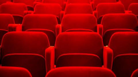 A shot of a rows of empty red chairs in a theatre