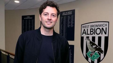 Ryan Mason stands at the top of some stairs inside The Hawthorns with the West Bromwich Albion club crest in the background on the wall