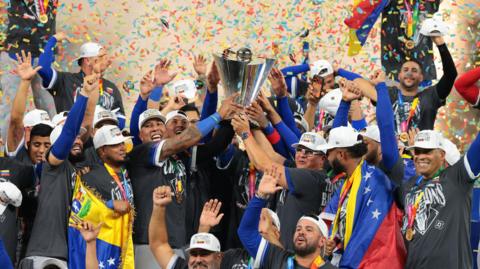 The Venezuelan team smiling and cheering holding a silver cup with rainbow confetti above their heads.