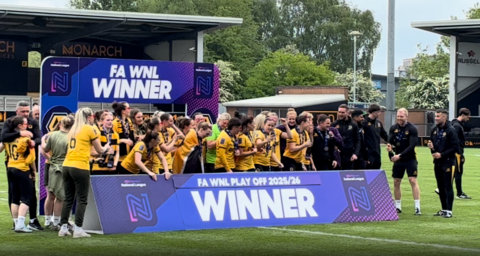 Wolves players pose with the WNL play-off winners banner on a pitch