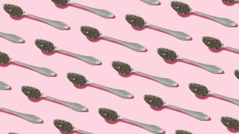 Diagonal silver teaspoons with chia seeds on them on a pink background.