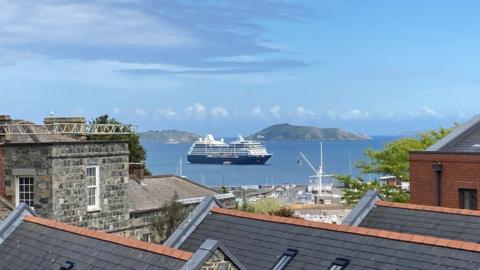 Spirit of the Seas Cruise ship out at sea, through the roof tops. Pictured in front of two smaller islands, Herm and Jethou.