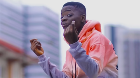 Nigerian singer Afeez Adesina, popularly known as Destiny Boy wearing a pink and purple jumper.  Here he is seen performing in his music video Time Is Money.

