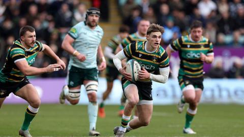 Archie McParland runs with ball in hand for Northampton Saints against Leicester Tigers. Various Saints' and Leicester players can be seen in the background.